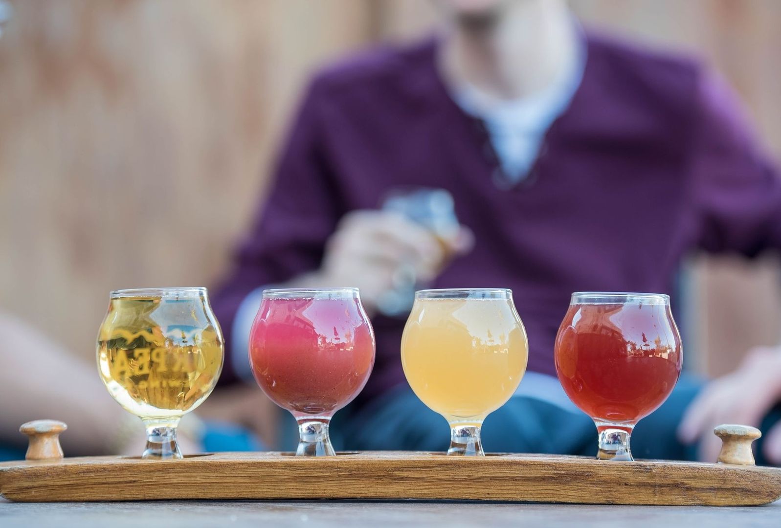 Fyra färgglada drycker i glas på en träbricka för provsmakning